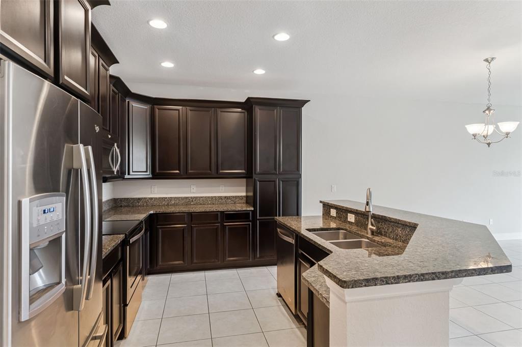 A kitchen features dark wood cabinets, granite countertops, stainless steel appliances, and light tile flooring — 10738 BELFRY CIRCLE, ORLANDO, FL