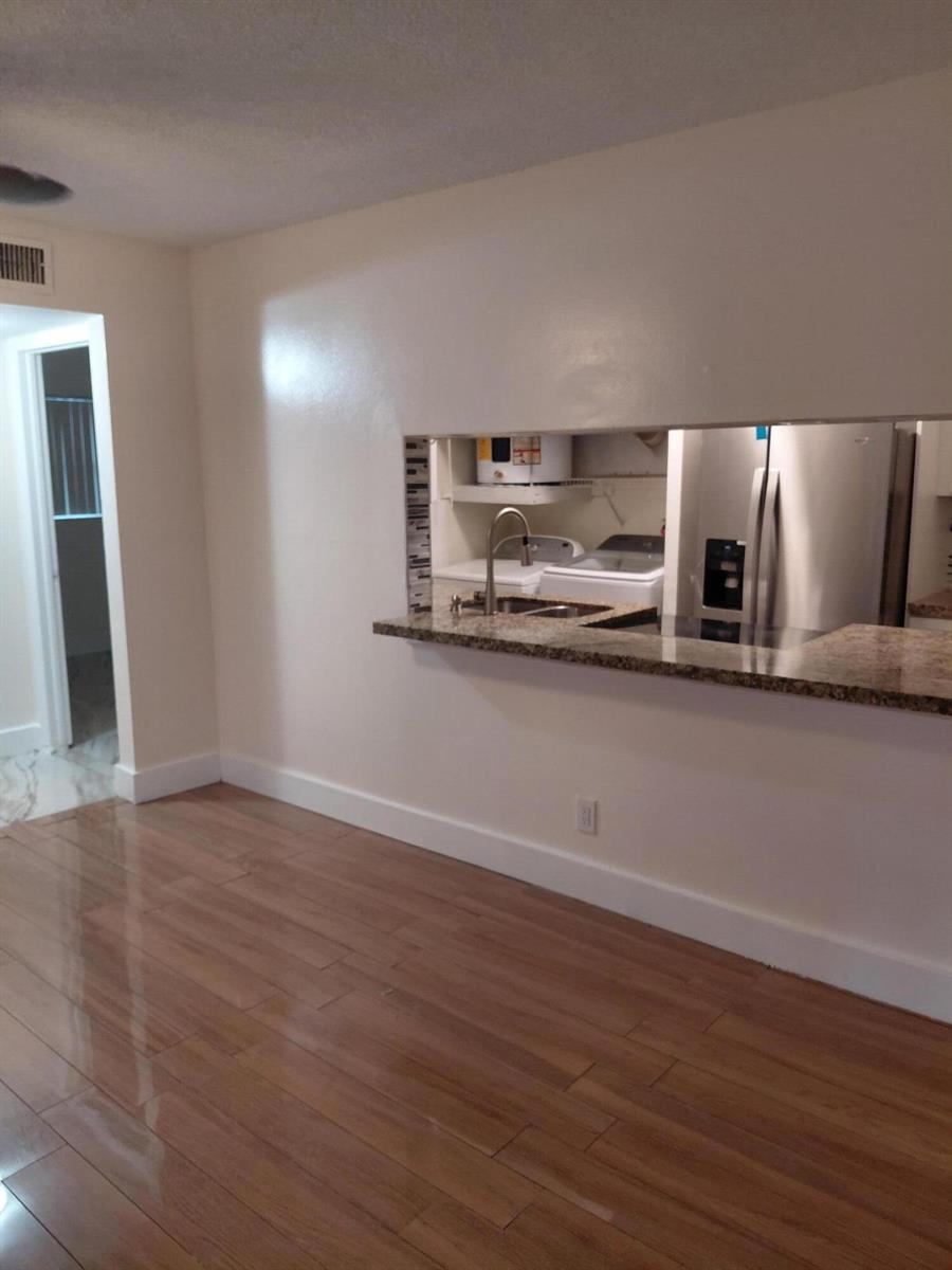 A room with wood-look flooring features a pass-through window looking into a kitchen area — 4525 NW Treehouse Lane # A, Tamarac FL 33319, TAMARAC, FL