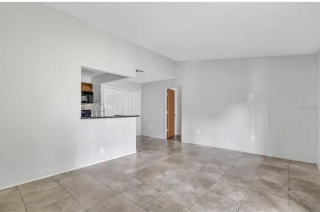An open-concept living area features light gray walls, large neutral floor tiles, and a kitchen — 3827 BAY CLUB CIRCLE UNIT 204, KISSIMMEE, FL