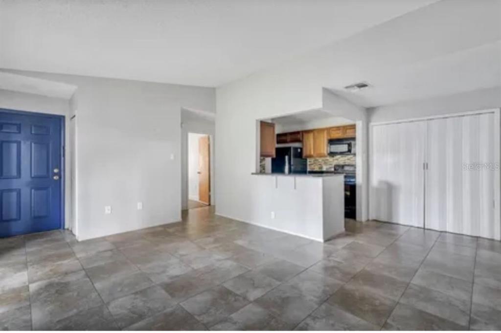 An open-concept living area features tile flooring, a blue front door, and a kitchen pass-through — 3827 BAY CLUB CIRCLE UNIT 204, KISSIMMEE, FL
