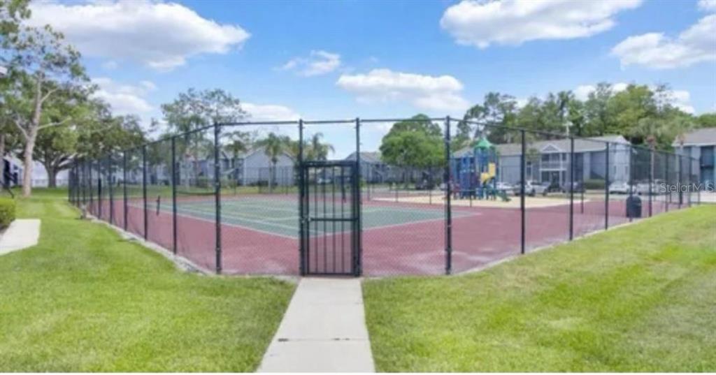 A fenced tennis court sits next to a playground in an apartment complex courtyard — 3827 BAY CLUB CIRCLE UNIT 204, KISSIMMEE, FL