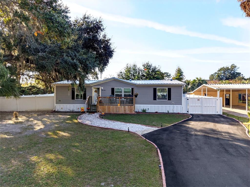 A single-story manufactured home with grey siding, a wooden deck, and a paved driveway — 15068 SE 105TH AVENUE, SUMMERFIELD, FL