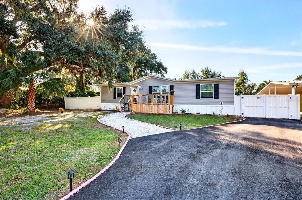 A single-story manufactured home with a wooden deck, white fence, and paved driveway — 15068 SE 105TH AVENUE, SUMMERFIELD, FL