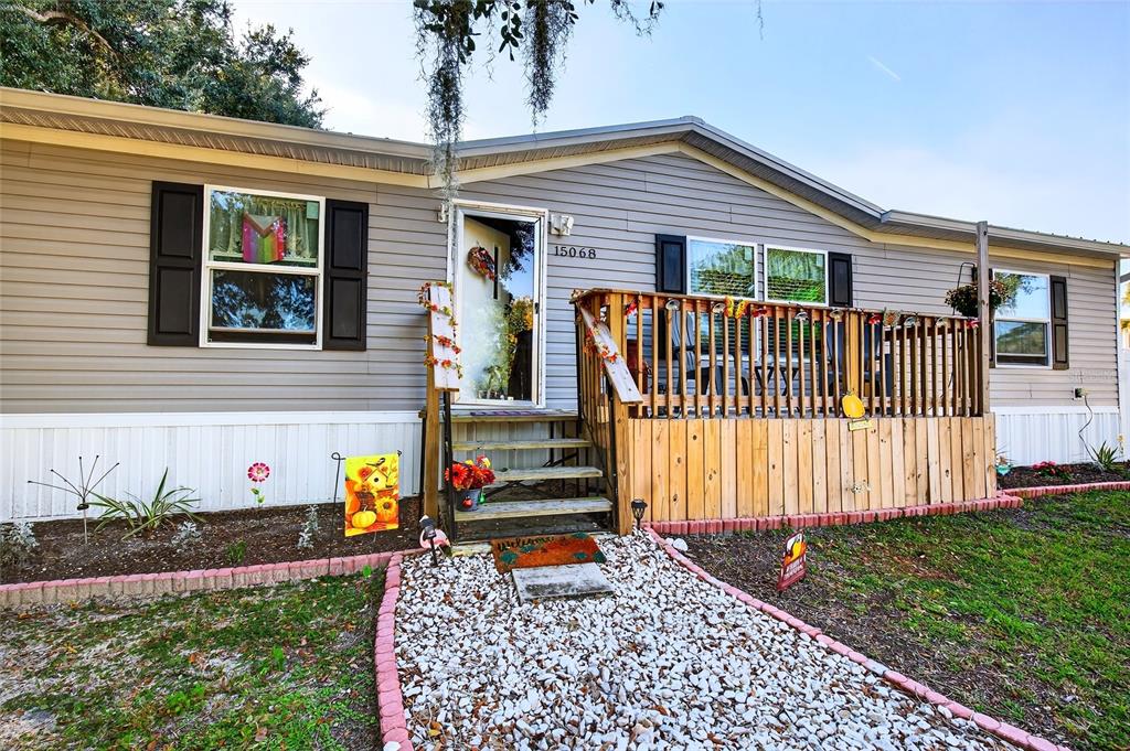 A single-story manufactured home with light gray siding, a wooden front deck, and gravel path — 15068 SE 105TH AVENUE, SUMMERFIELD, FL