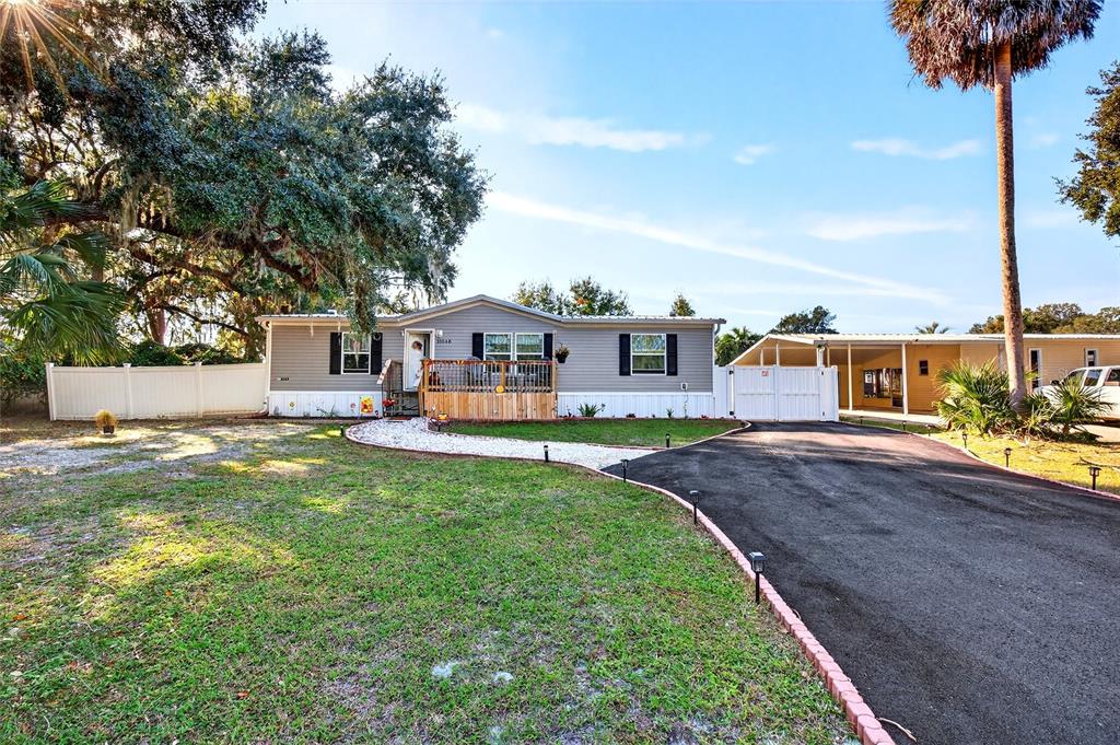 A single-story manufactured home features a wooden deck, white vinyl fencing, and an asphalt driveway — 15068 SE 105TH AVENUE, SUMMERFIELD, FL