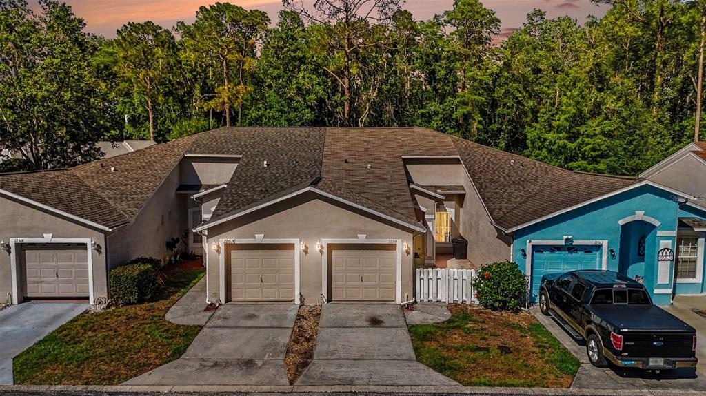 An aerial view shows three attached residential units with garages and driveways in front of trees — 12514 HOLLYBROOK LANE, HUDSON, FL