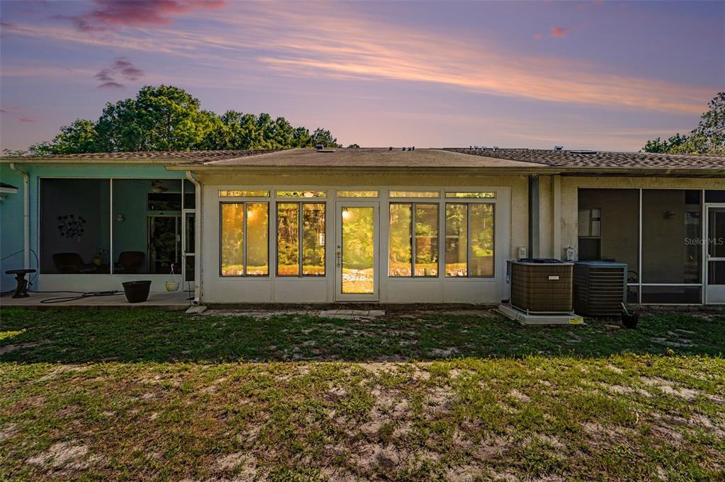 The rear exterior of a house features a central sunroom flanked by screened-in porches — 12514 HOLLYBROOK LANE, HUDSON, FL