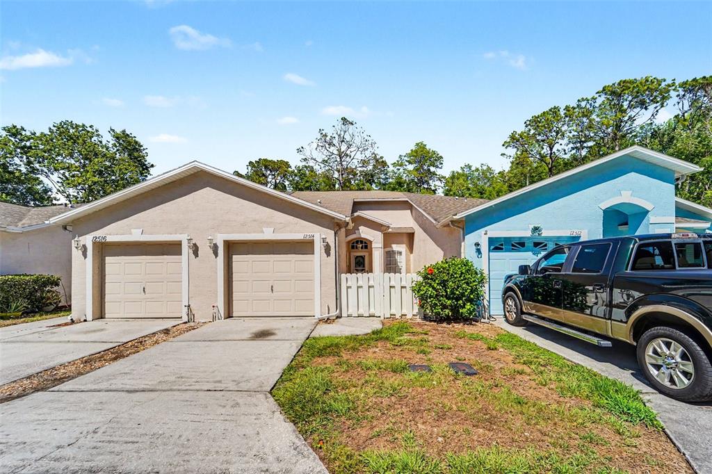 A tan and blue duplex features three garage doors and a shared front entryway — 12514 HOLLYBROOK LANE, HUDSON, FL
