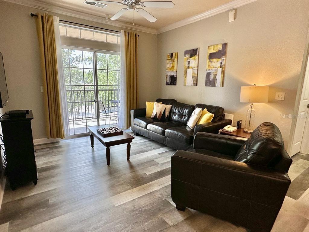 A living room features a dark leather sofa and armchair, wood-look flooring, and a balcony door — 1301 TUSCAN TERRACE UNIT 9301, DAVENPORT, FL