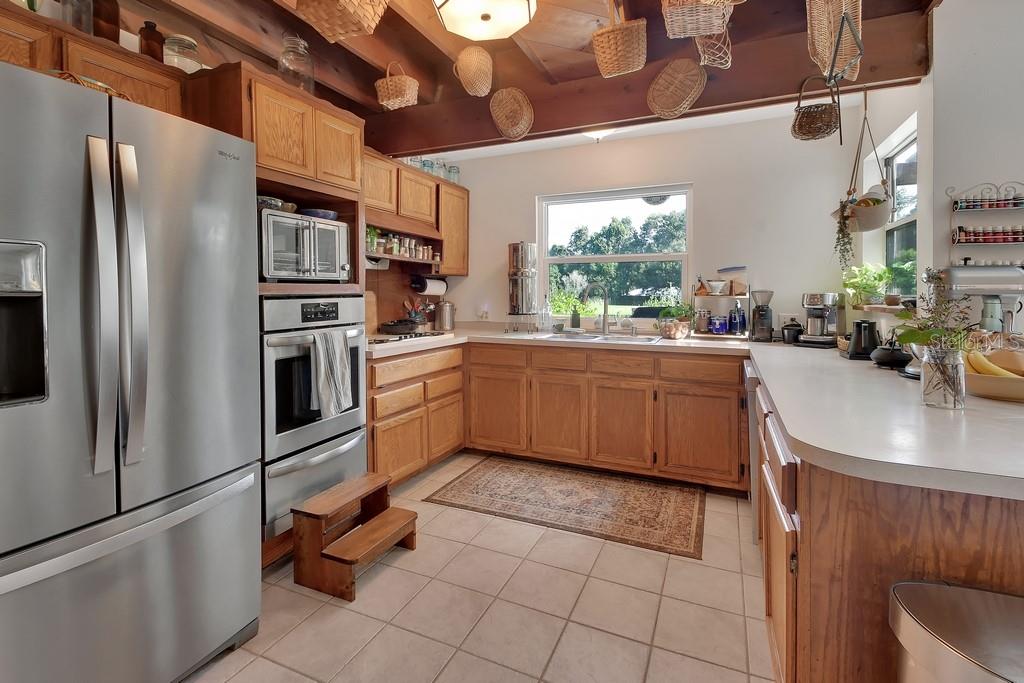 A kitchen features oak cabinets, stainless steel appliances, tile flooring, and baskets hanging from beams — 1379 TAYLOR ROAD W, DELAND, FL