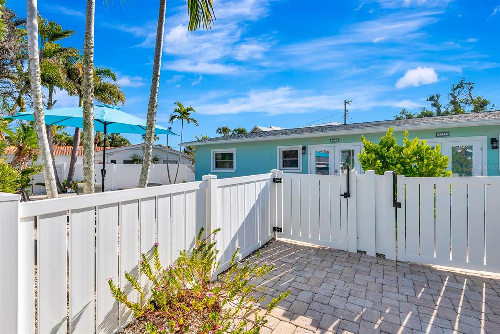 A white vinyl fence encloses a paved patio area in front of a light blue house — 207 75TH STREET UNIT B, BRADENTON BEACH, FL