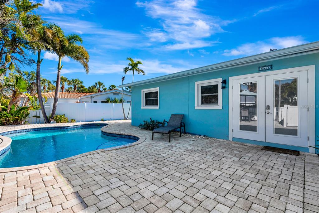 A turquoise house exterior features a swimming pool and a paved patio with a lounge chair — 207 75TH STREET UNIT B, BRADENTON BEACH, FL