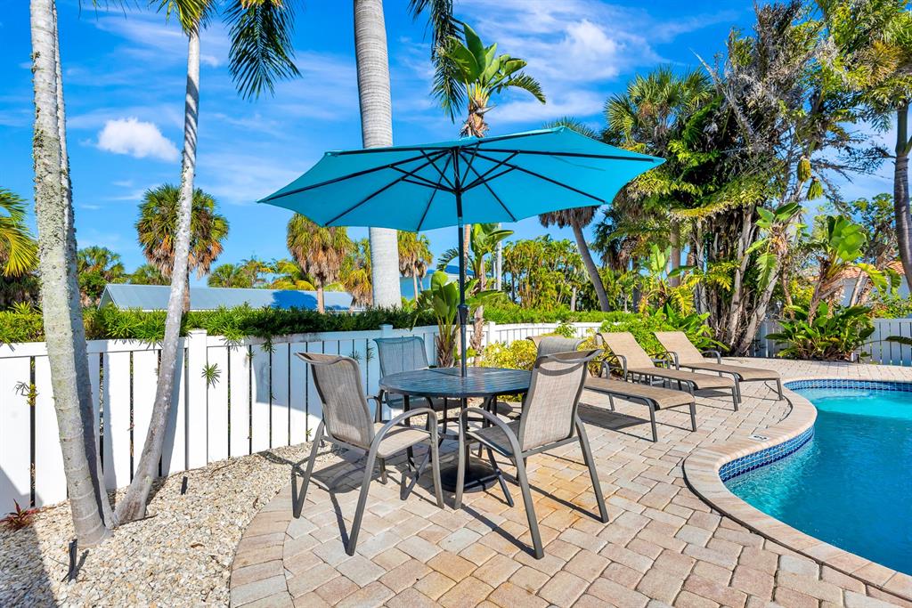 A patio with a dining set, blue umbrella, and lounge chairs beside a swimming pool — 207 75TH STREET UNIT B, BRADENTON BEACH, FL