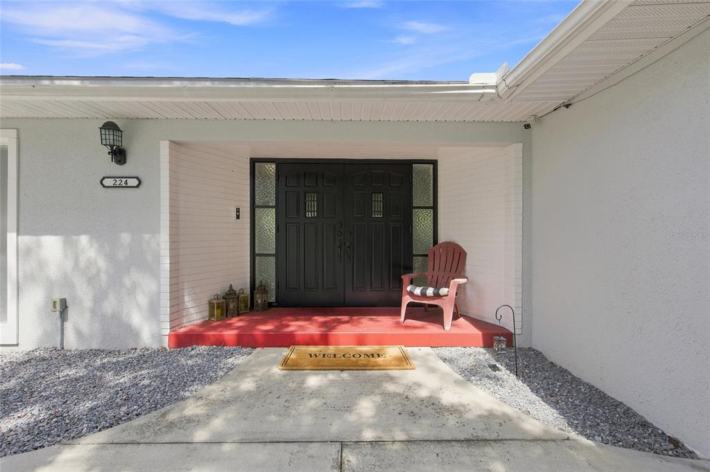 A front entryway features a red porch, double black doors, and a single plastic chair — 224 N MCGOWAN AVENUE, CRYSTAL RIVER, FL