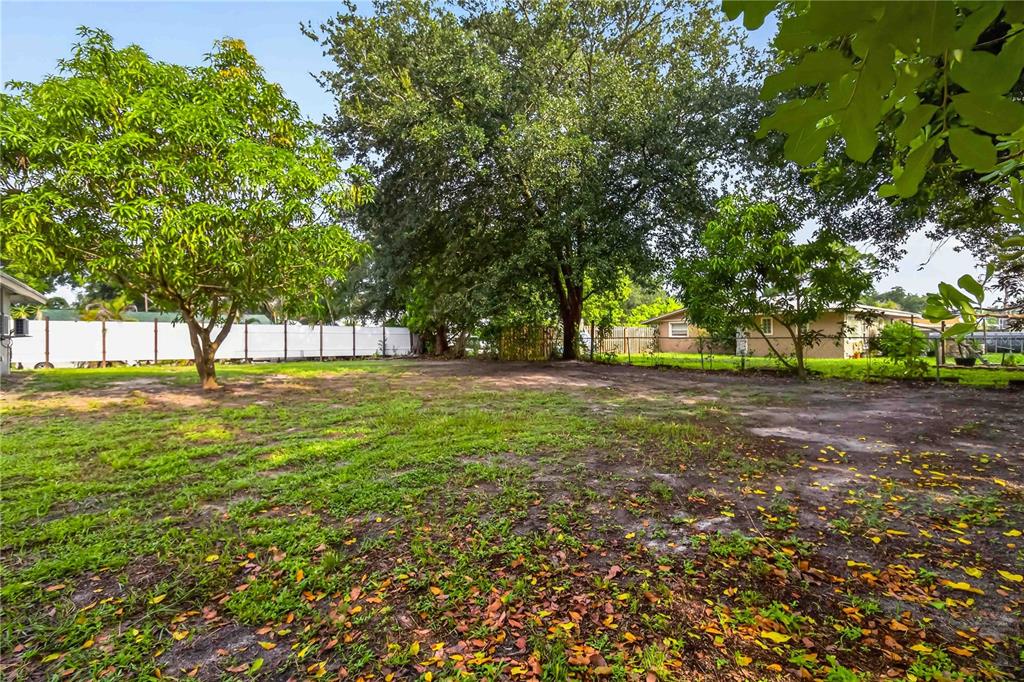 A large, grassy backyard features several mature trees and a white privacy fence — 4734 DELMONTE AVENUE, SARASOTA, FL