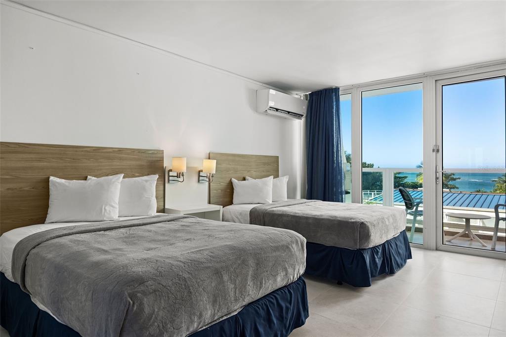A hotel room with two beds, wood headboards, and a balcony overlooking the ocean — 6165 ISLA VERDE AVE. UNIT 377, CAROLINA, PR