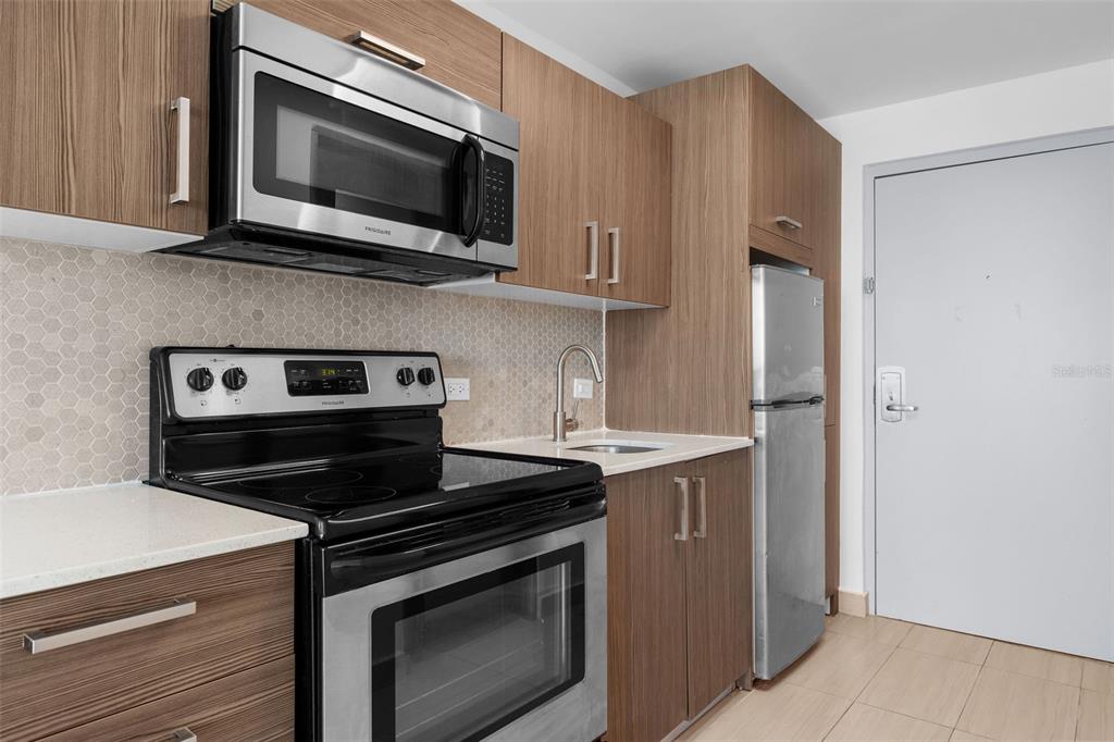 A kitchen featuring wood-grain cabinets, stainless steel appliances, and a light-colored tile backsplash — 6165 ISLA VERDE AVE. UNIT 377, CAROLINA, PR