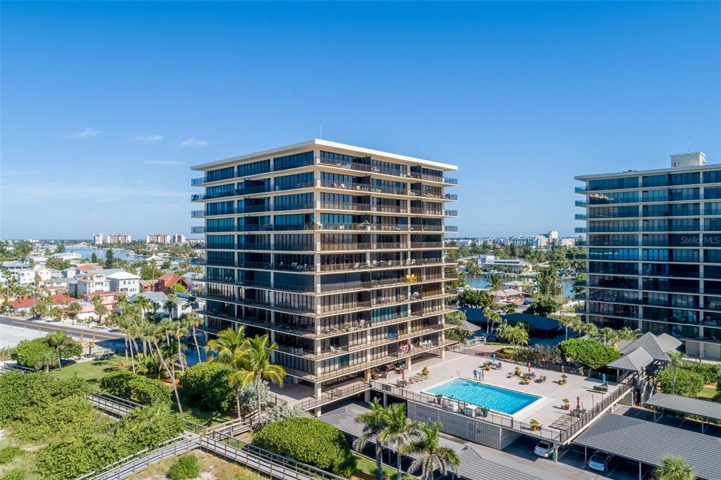 An aerial view shows a multi-story residential building with balconies, a pool, and parking — 7650 BAYSHORE DRIVE UNIT 606, TREASURE ISLAND, FL
