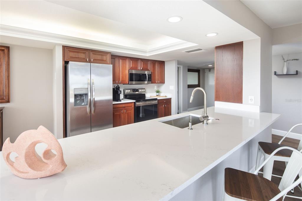 A kitchen features a large white quartz island, stainless steel appliances, and wood cabinetry — 7650 BAYSHORE DRIVE UNIT 606, TREASURE ISLAND, FL