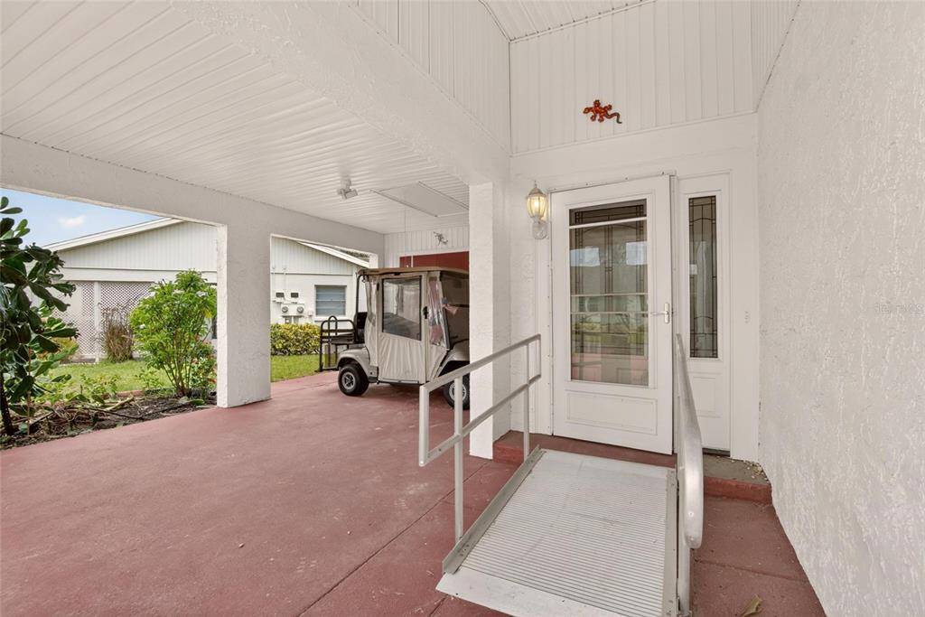 A covered patio features a wheelchair ramp leading to a white front door and a golf cart — 213 GLENELLEN PLACE, SUN CITY CENTER, FL