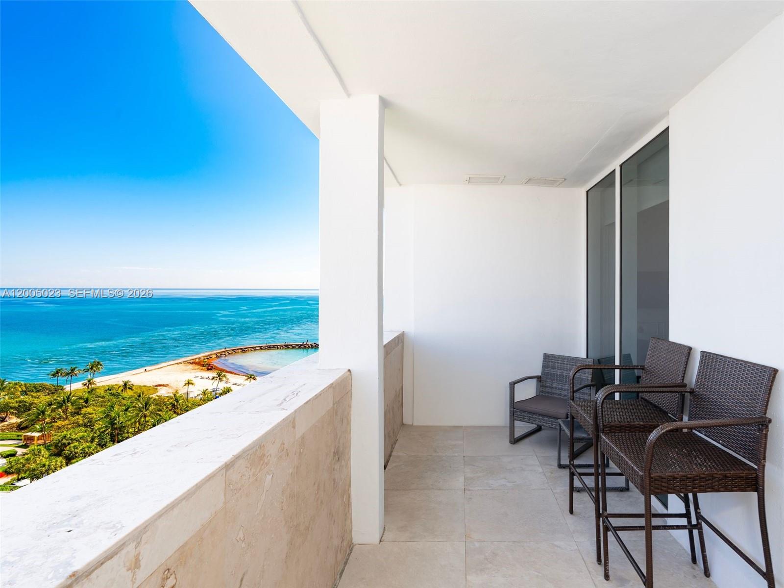 A balcony with wicker chairs overlooks a beach and the ocean — 10275 Collins Ave # 1502, Bal Harbour FL 33154, BAL HARBOUR, FL