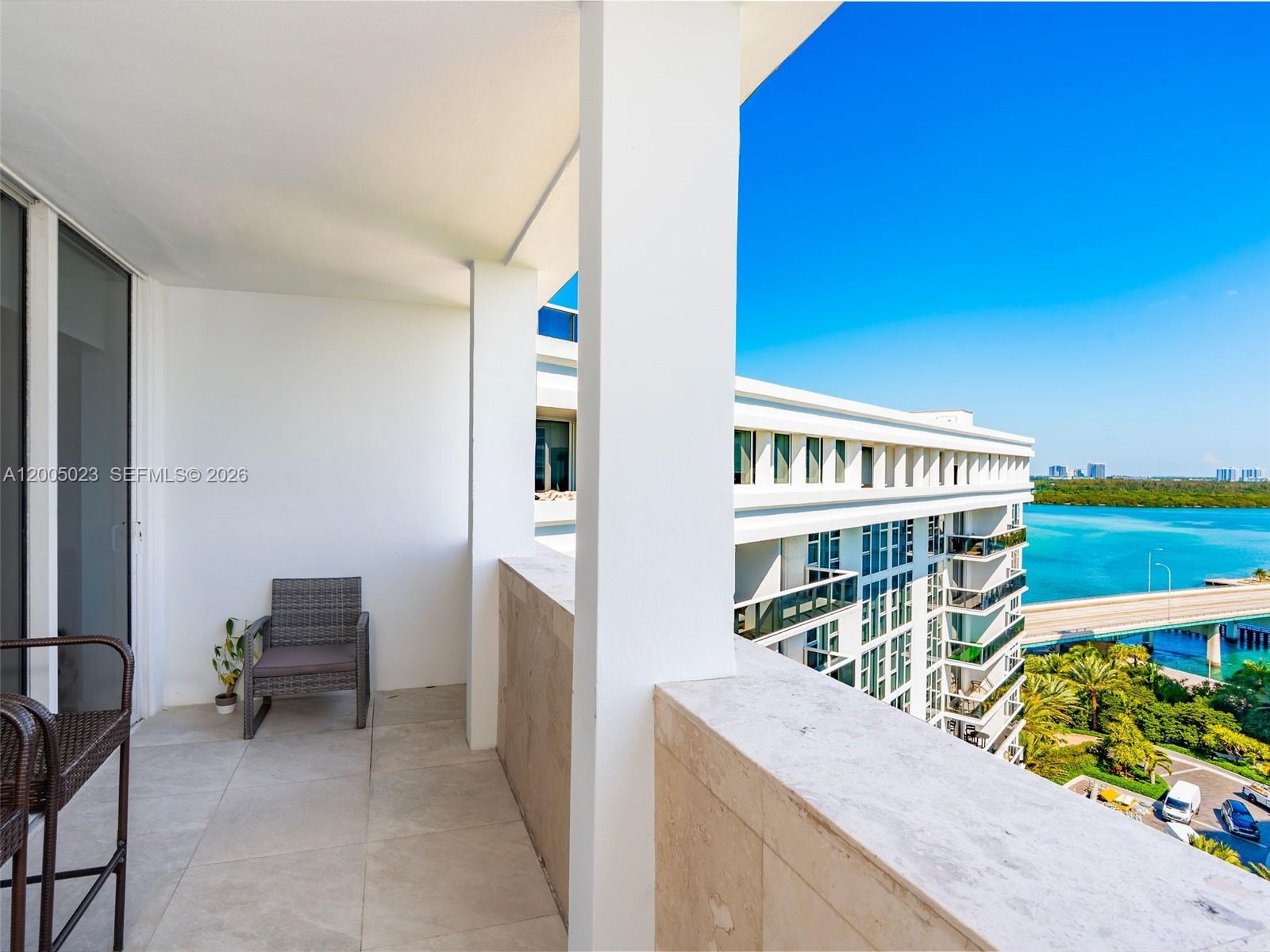 A balcony with tile flooring and a chair overlooks a nearby building and water — 10275 Collins Ave # 1502, Bal Harbour FL 33154, BAL HARBOUR, FL