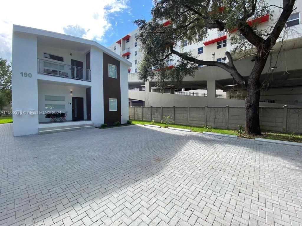 A two-story white building with a paved parking area stands next to a larger structure — 190 NW 57th St, Miami FL 33127, MIAMI, FL