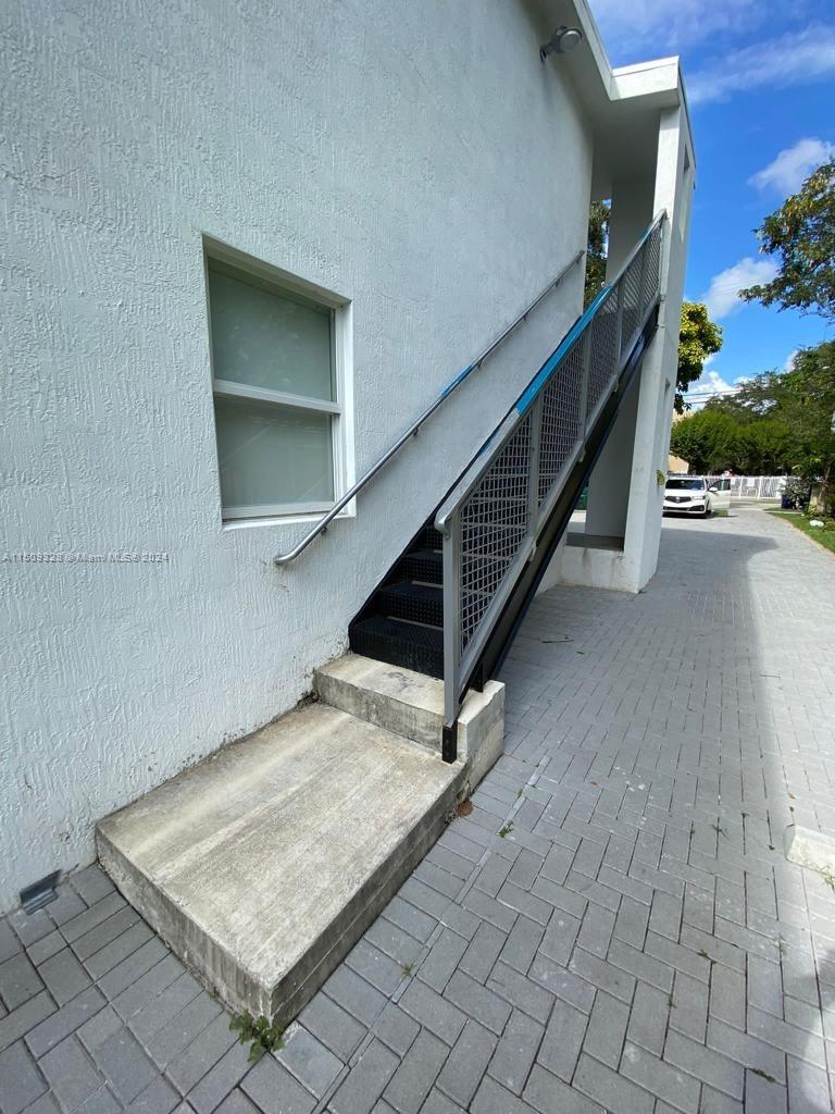 An exterior view shows a white building with a metal staircase leading to an upper level — 190 NW 57th St, Miami FL 33127, MIAMI, FL
