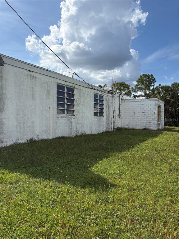 The exterior of a white concrete block building with louvered windows sits on a grassy lot — 1308 TAMIAMI TRAIL, PUNTA GORDA, FL