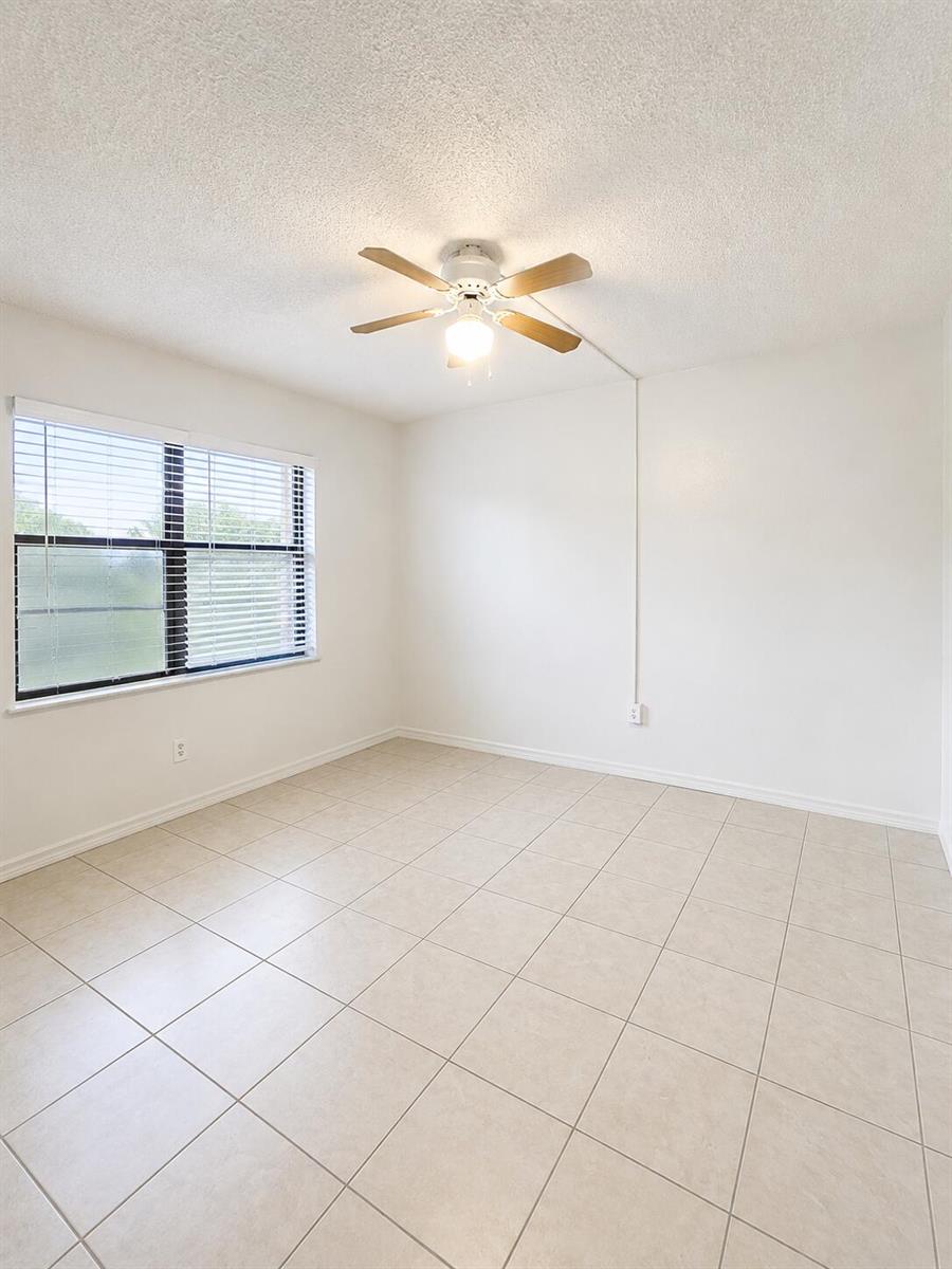 An empty room features white walls, beige tile flooring, a ceiling fan, and a window — 2050 Oleander Boulevard # 105, Fort Pierce FL 34950, FORT PIERCE, FL