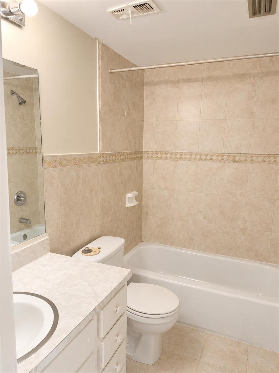 A bathroom features a vanity, a toilet, and a bathtub with beige tiled walls — 2050 Oleander Boulevard # 105, Fort Pierce FL 34950, FORT PIERCE, FL