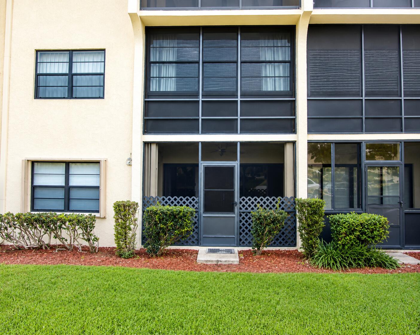 A ground-level apartment exterior features a screened patio, dark window frames, and manicured landscaping — 2050 Oleander Boulevard # 105, Fort Pierce FL 34950, FORT PIERCE, FL