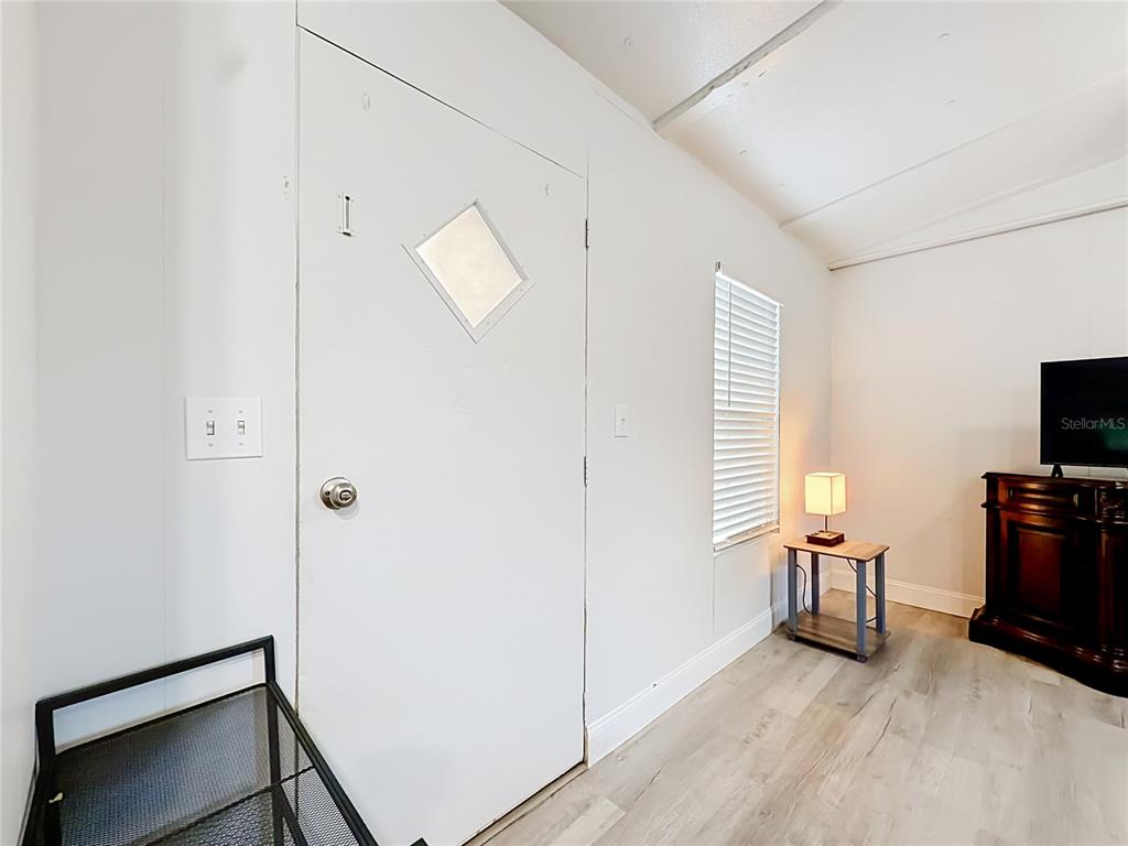 A room with white walls, light wood-look flooring, a white door, and a television console — 5396 W RICHLAND LANE, HOMOSASSA, FL
