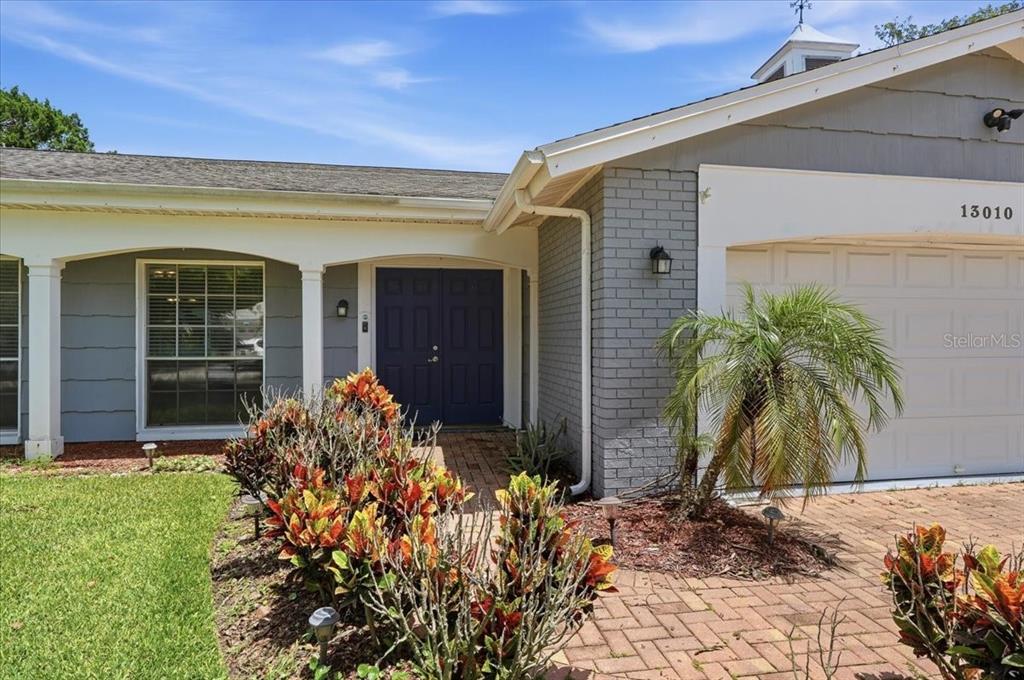 The exterior of a house features a brick facade, a covered porch, and a paved walkway — 13010 PEBBLE BEACH CIRCLE, HUDSON, FL
