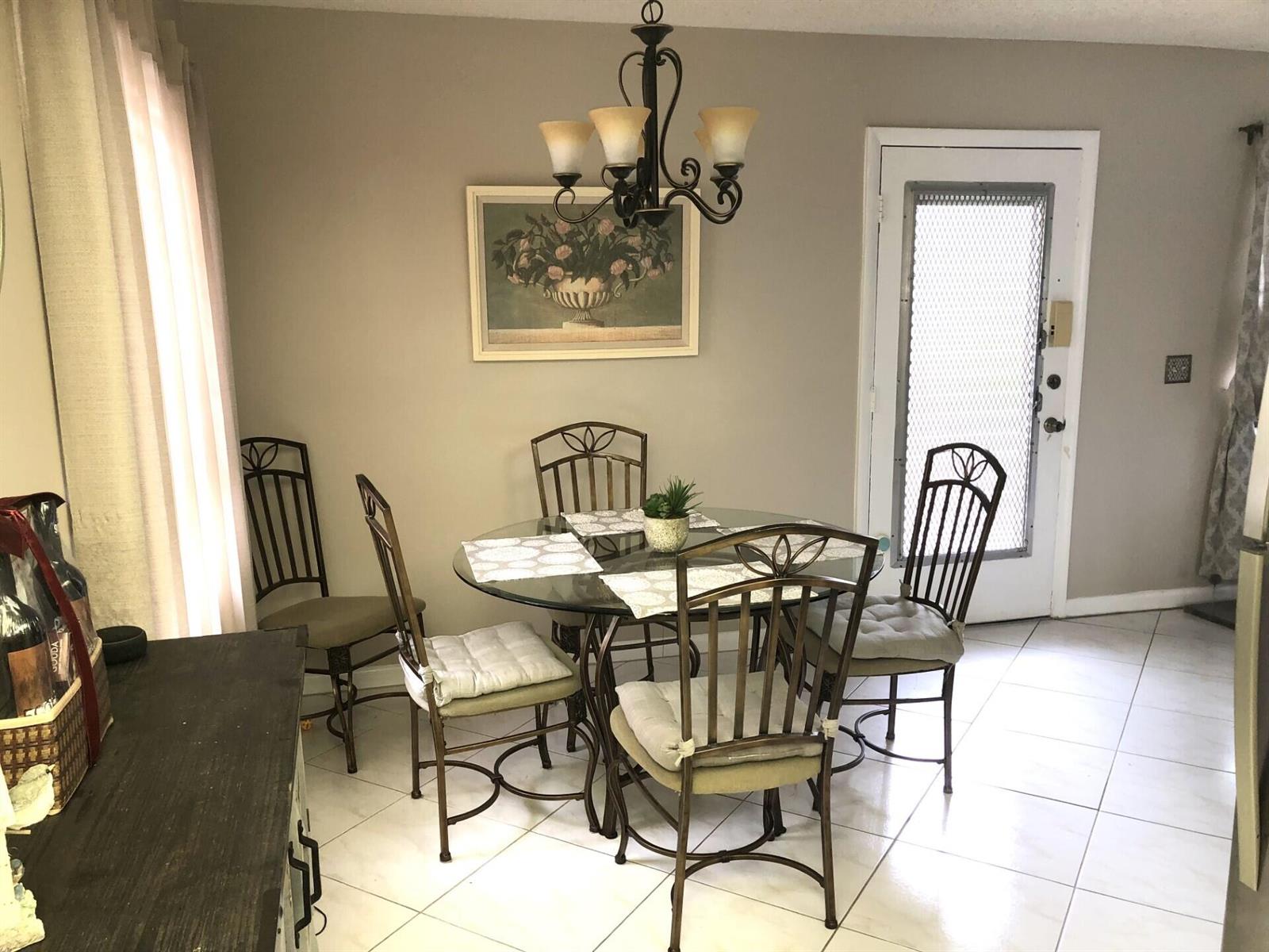 A dining area features a glass-topped table with four metal chairs and a chandelier — 499 Piedmont K, Delray Beach FL 33484, DELRAY BEACH, FL