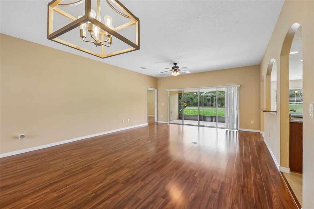 A spacious living room with hardwood floors, a ceiling fan, and a view of greenery — 4025 ARLINGTON RIDGE BOULEVARD, LEESBURG, FL