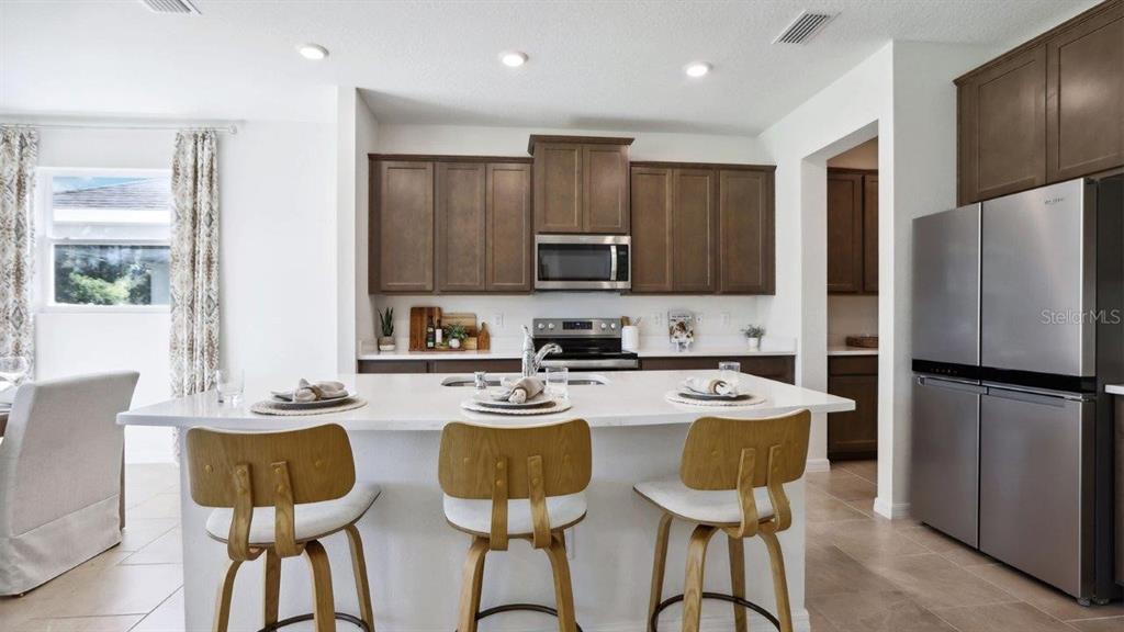 A modern kitchen features dark wood cabinets, stainless steel appliances, and a white island — 6861 FLINT CREEK DRIVE, LAND O LAKES, FL