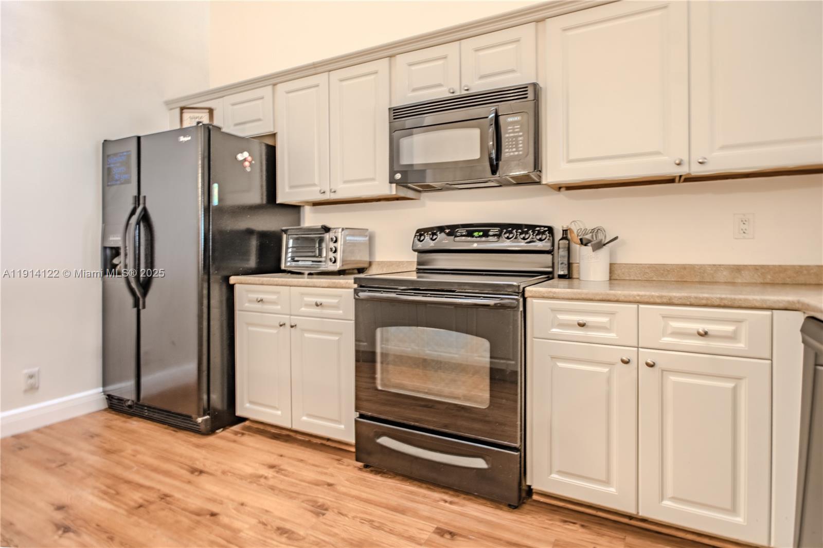 A kitchen features light-colored cabinets, black appliances, and wood-look flooring — 7652 S Pinewalk Dr S # 139, Margate FL 33063, MARGATE, FL