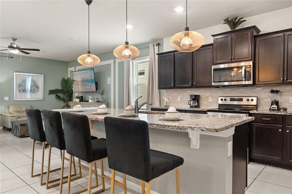 A kitchen with dark cabinets, granite countertops, and a breakfast bar with four black stools — 2036 LELANI CIR, DAVENPORT, FL