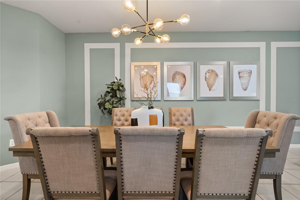 A dining room features a wooden table, tufted chairs, shell artwork, and a modern chandelier — 2036 LELANI CIR, DAVENPORT, FL
