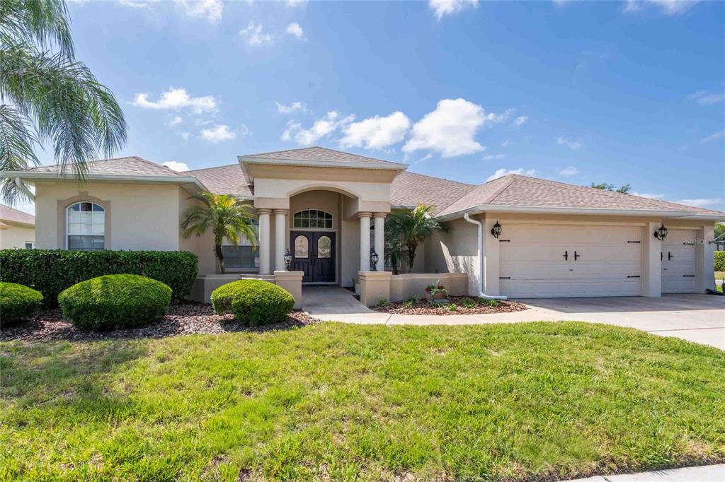 A single-story beige house with a three-car garage and a covered arched entryway — 7425 MELOGOLD CIRCLE, LAND O LAKES, FL