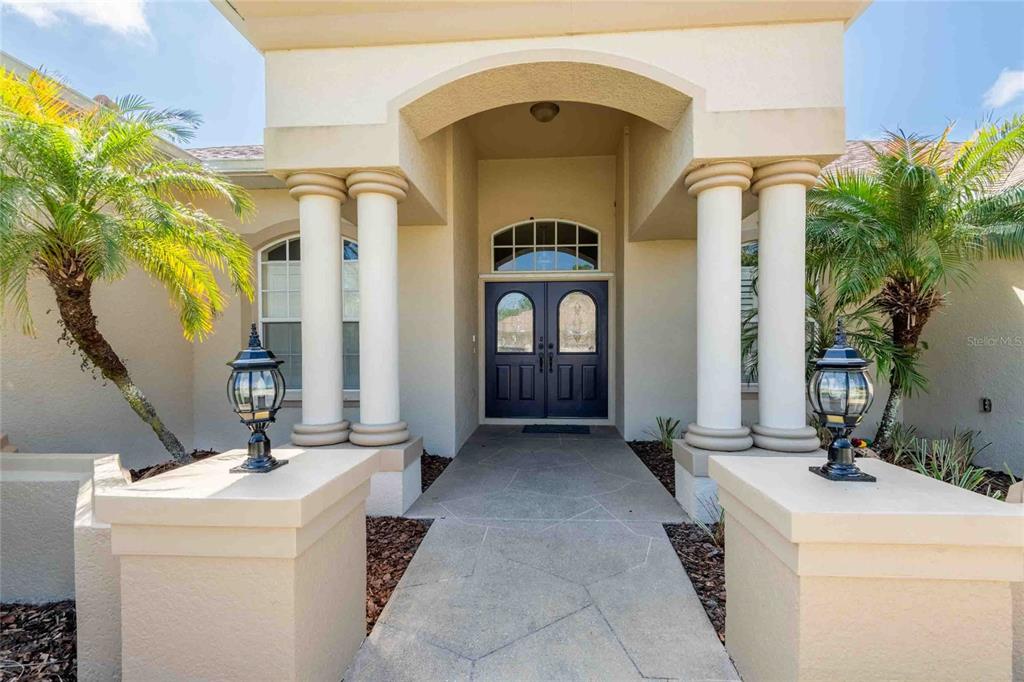 A paved walkway leads to a double front door framed by four white columns — 7425 MELOGOLD CIRCLE, LAND O LAKES, FL