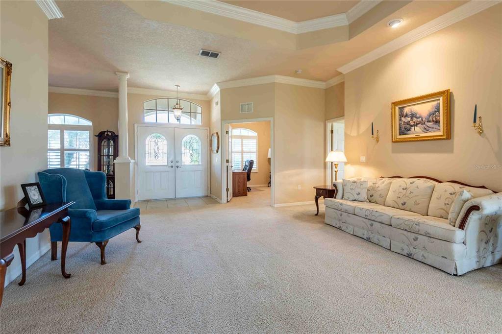A living room features beige carpet, a floral sofa, a blue armchair, and double entry doors — 7425 MELOGOLD CIRCLE, LAND O LAKES, FL