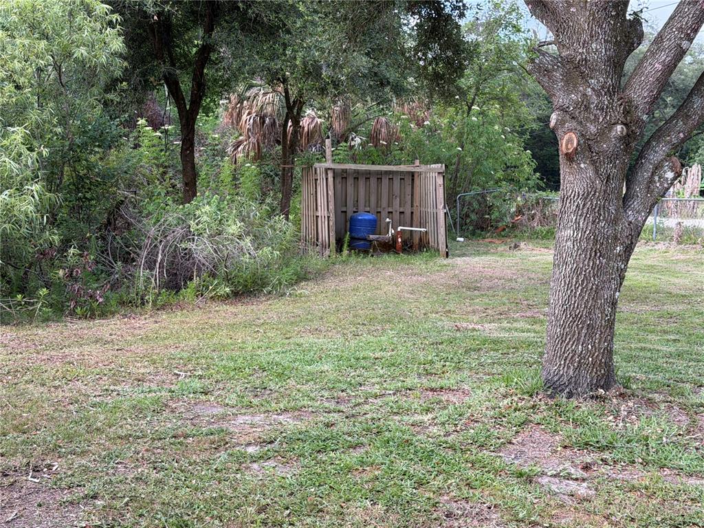 A blue water pressure tank sits inside a wooden enclosure in a grassy yard — 8336 HAMSTER DRIVE, ZEPHYRHILLS, FL