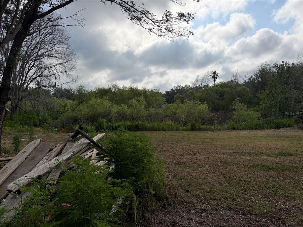 A pile of wooden boards sits in the foreground of a large, grassy vacant lot — 8336 HAMSTER DRIVE, ZEPHYRHILLS, FL