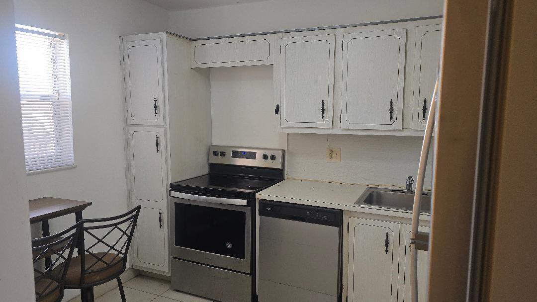 A kitchen features white cabinets, stainless steel appliances, a sink, and a small dining area — 3251 Holiday Springs Boulevard # 302, Margate FL 33063, MARGATE, FL