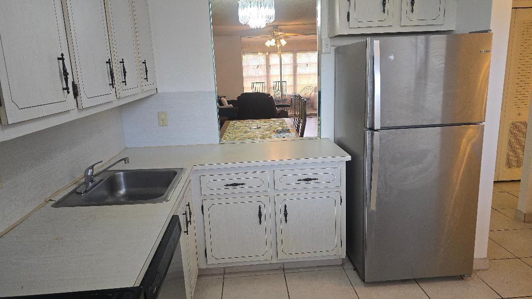 A kitchen features white cabinets, a stainless steel refrigerator, a sink, and a pass-through window — 3251 Holiday Springs Boulevard # 302, Margate FL 33063, MARGATE, FL
