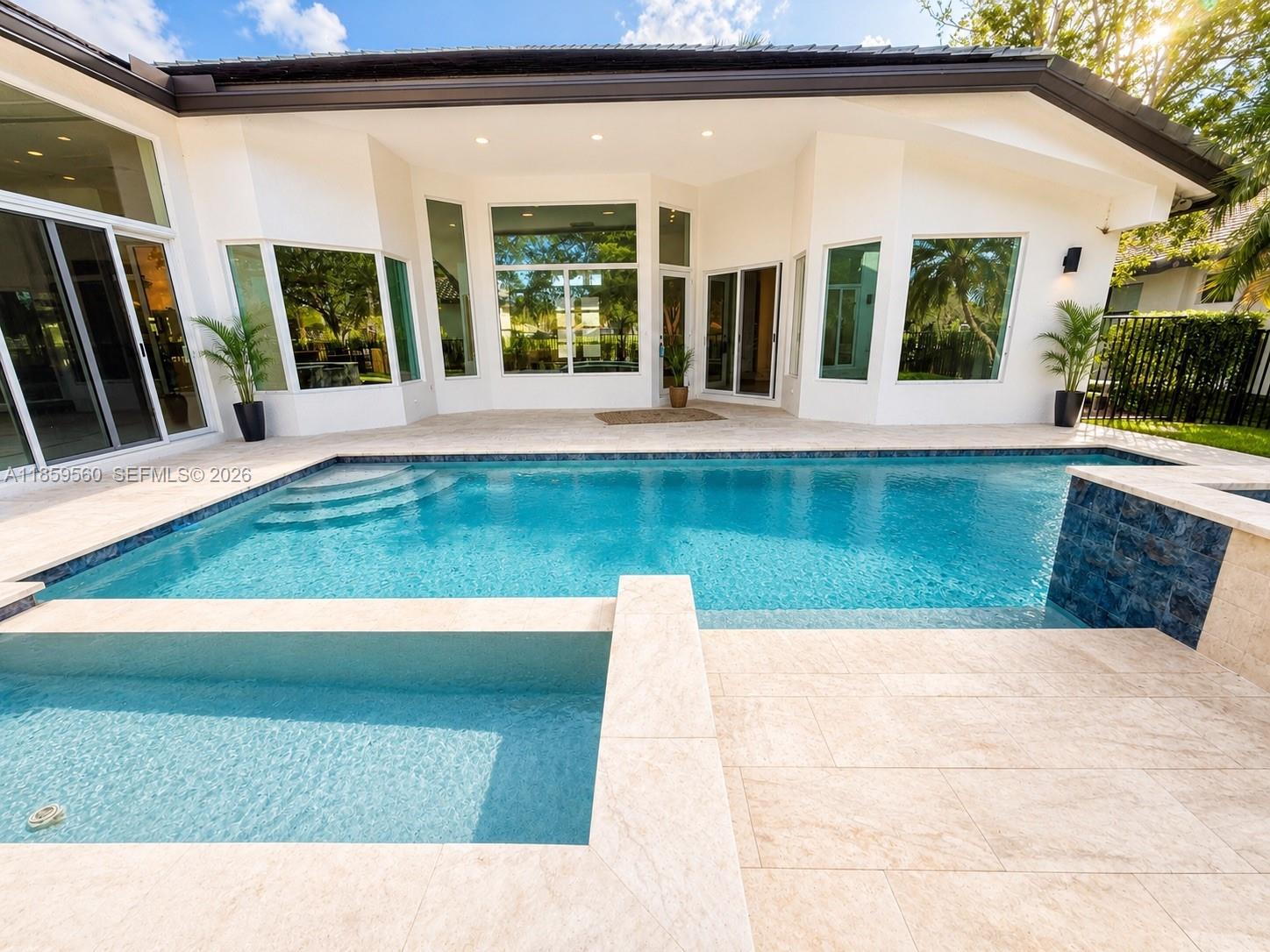 A backyard swimming pool and spa are situated on a stone patio behind a house — 2523 Montclaire Cir, Weston FL 33327, WESTON, FL