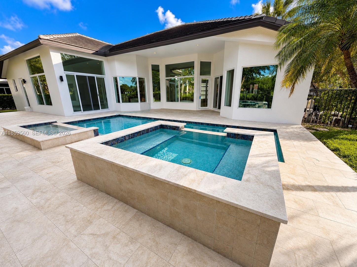 A modern house exterior features a raised spa and swimming pool with travertine decking — 2523 Montclaire Cir, Weston FL 33327, WESTON, FL
