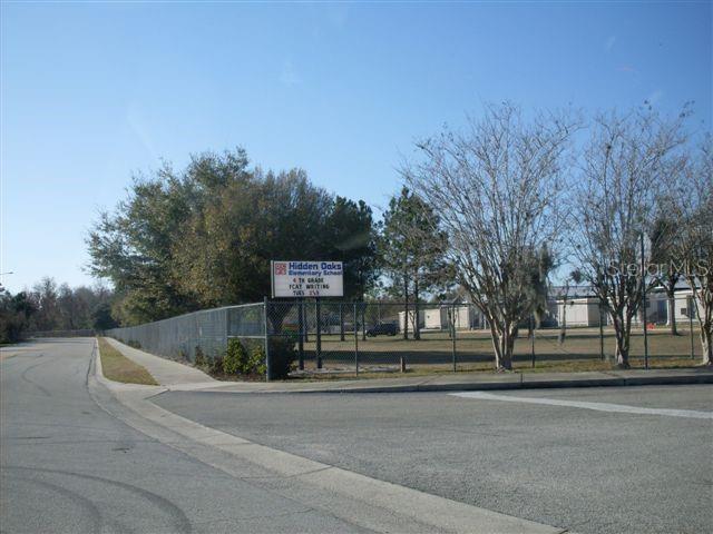 A chain-link fence surrounds the Hidden Oaks Elementary School grounds and its sign — SUBURBAN DRIVE, ORLANDO, FL